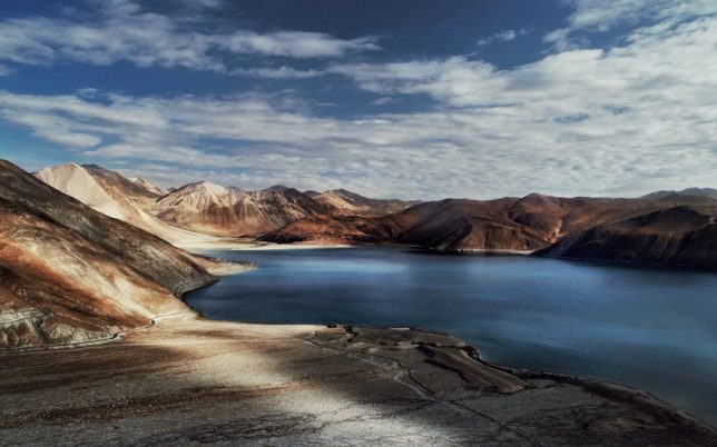 Spectacular landscape of rough rocky hills near pond under blue cloudy sky in countryside in sunny day